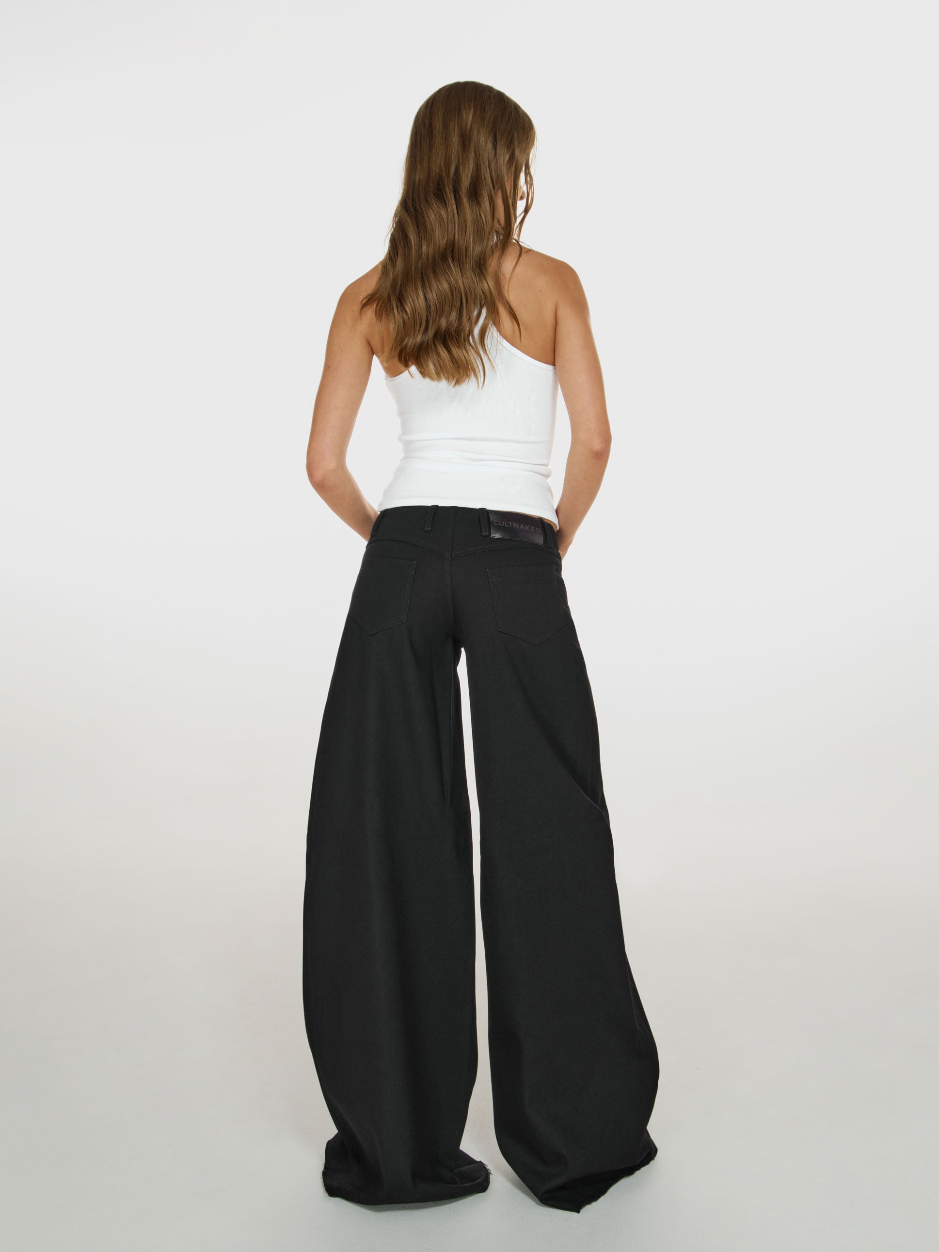 Full shot of a girl facing back in a white viscose tank top and black wide leg jeans with low rise