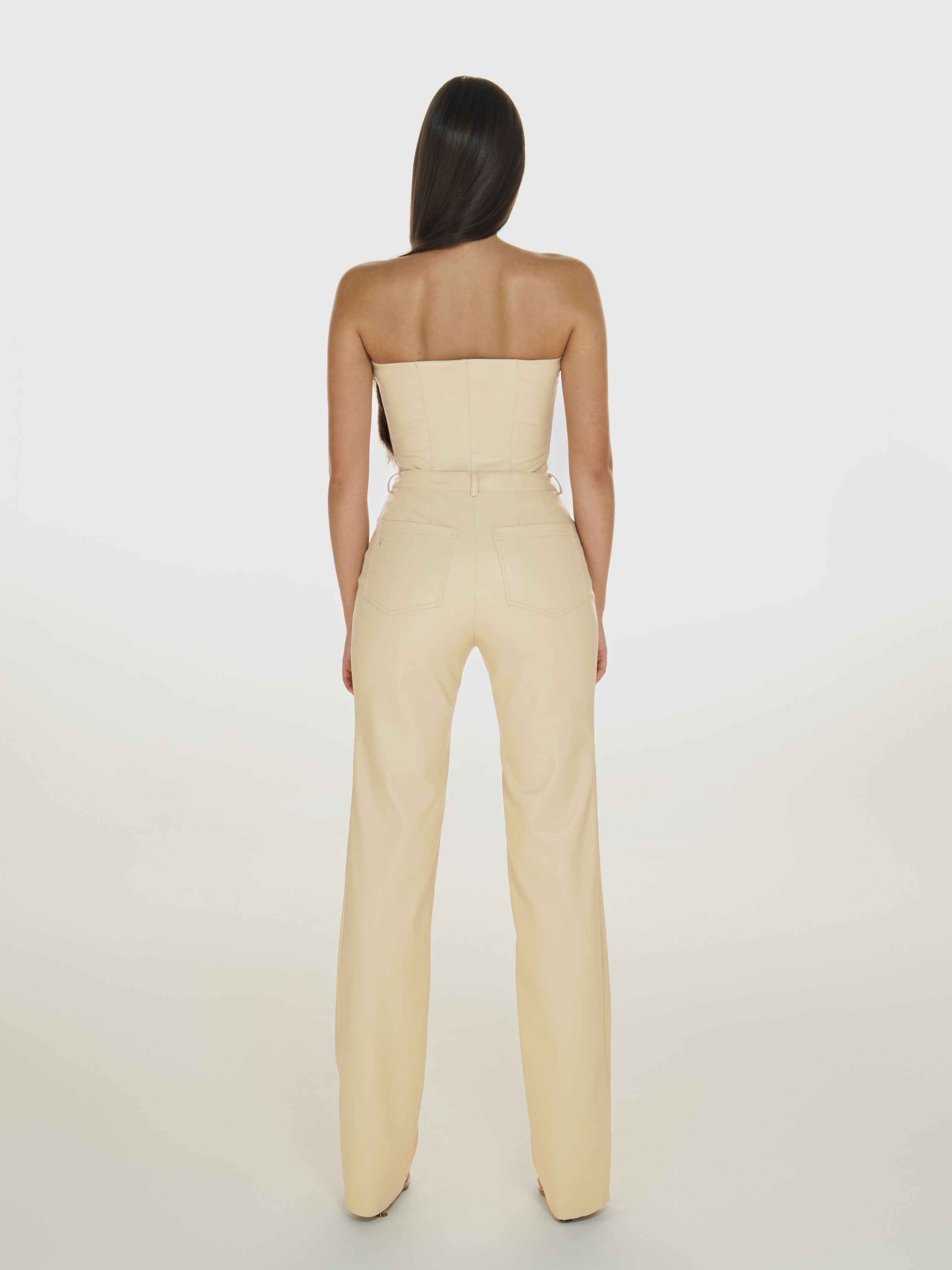 Full shot of a girl facing back in a cream vegan leather tube top and cream vegan leather pants with straight leg