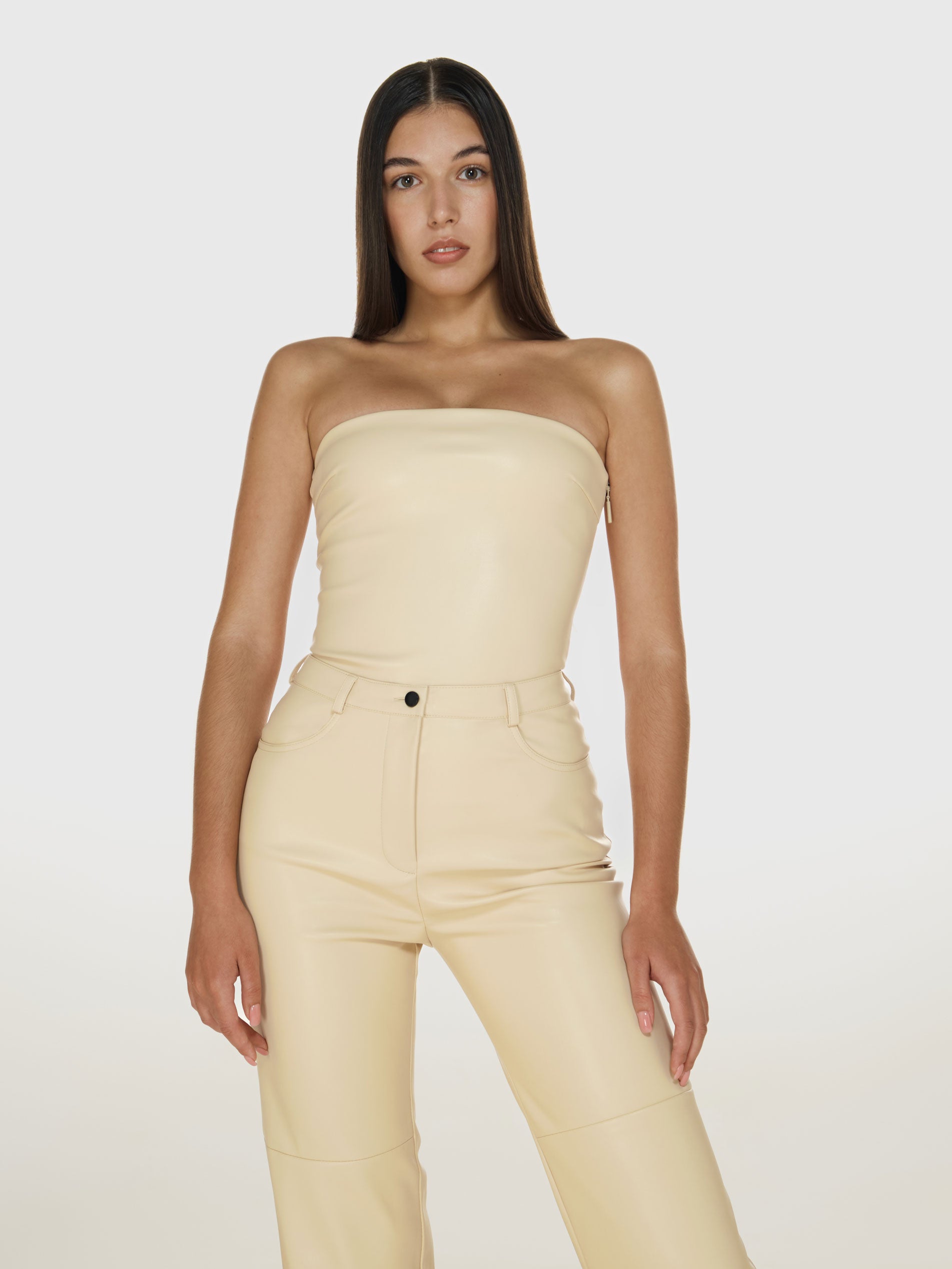 Cowboy shot of a girl in a cream vegan leather tube top and cream vegan leather pants with straight leg