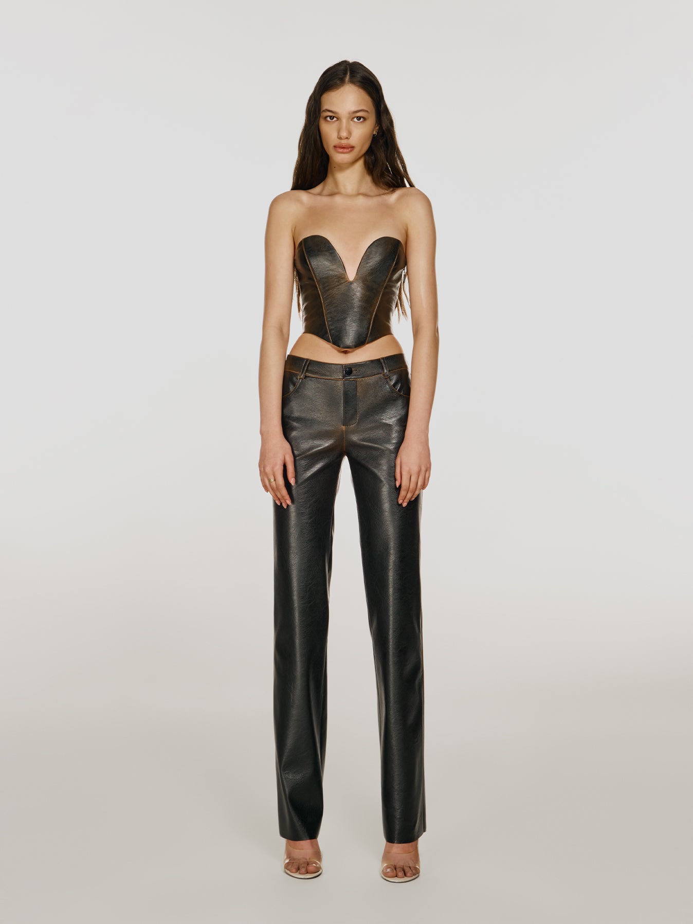 Full shot of a girl in a brown vegan leather tube top with deep v neck and brown vegan leather mid rise straight leg pants