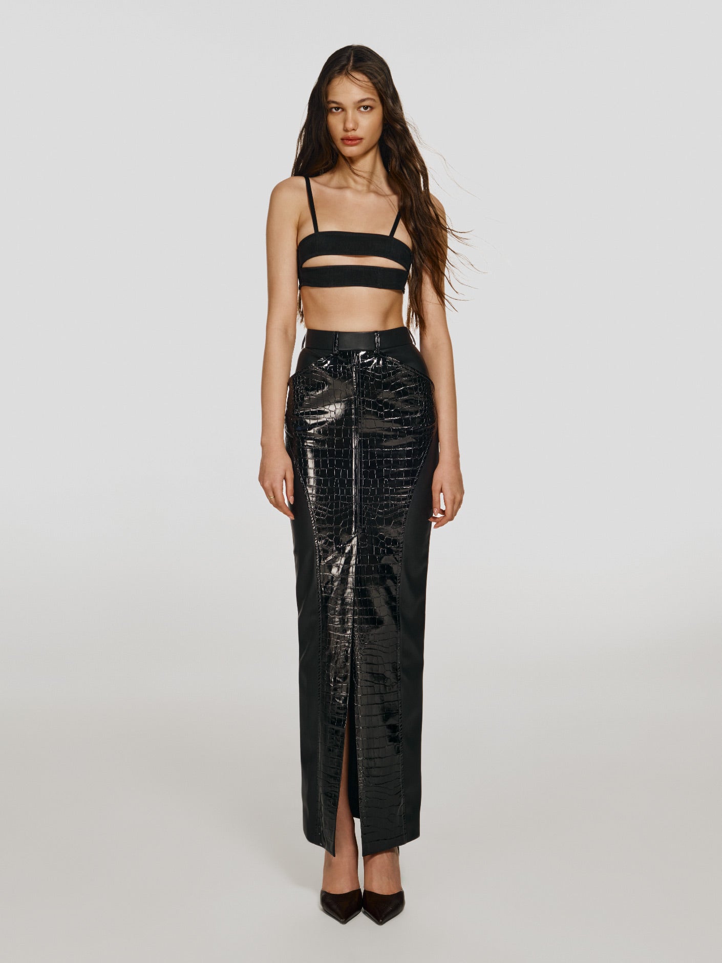 Full shot of a girl in a black mesh crop top with horizontal cut and a black vegan leather maxi skirt with high front slit