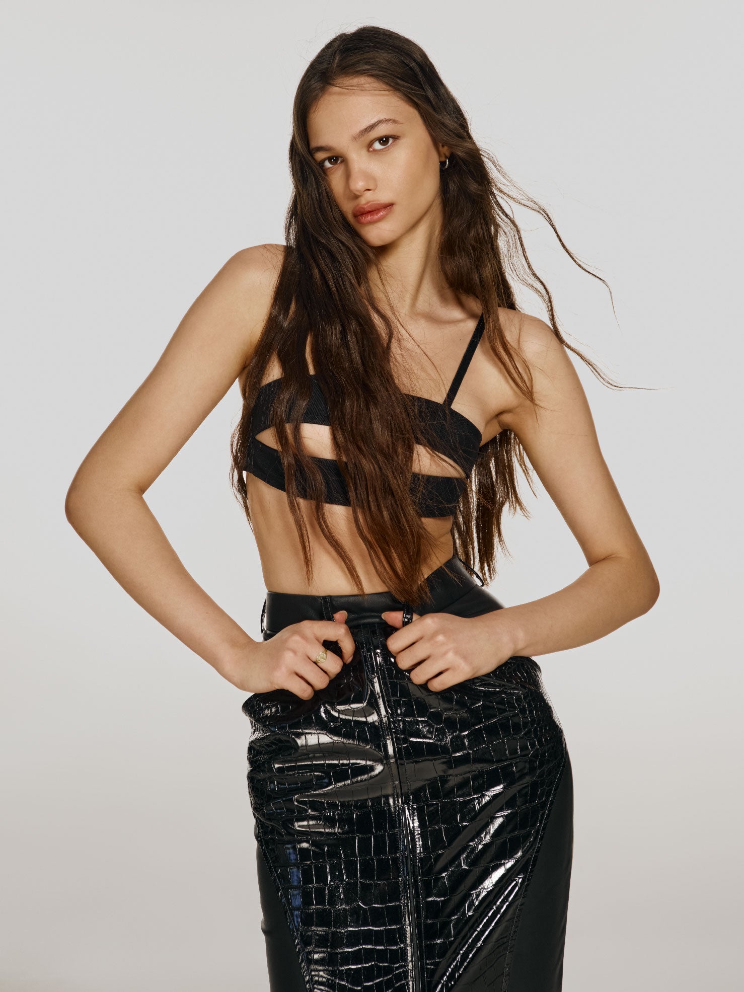 Cowboy shot of a girl in a black mesh crop top with a horizontal cut and a black vegan leather maxi skirt with a crocodile print 