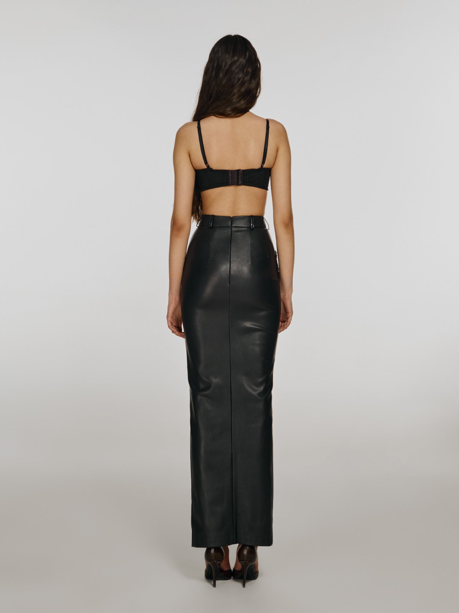 Full shot of a girl facing back in a black mesh crop top with horizontal cut and a black vegan leather skirt with high front slit