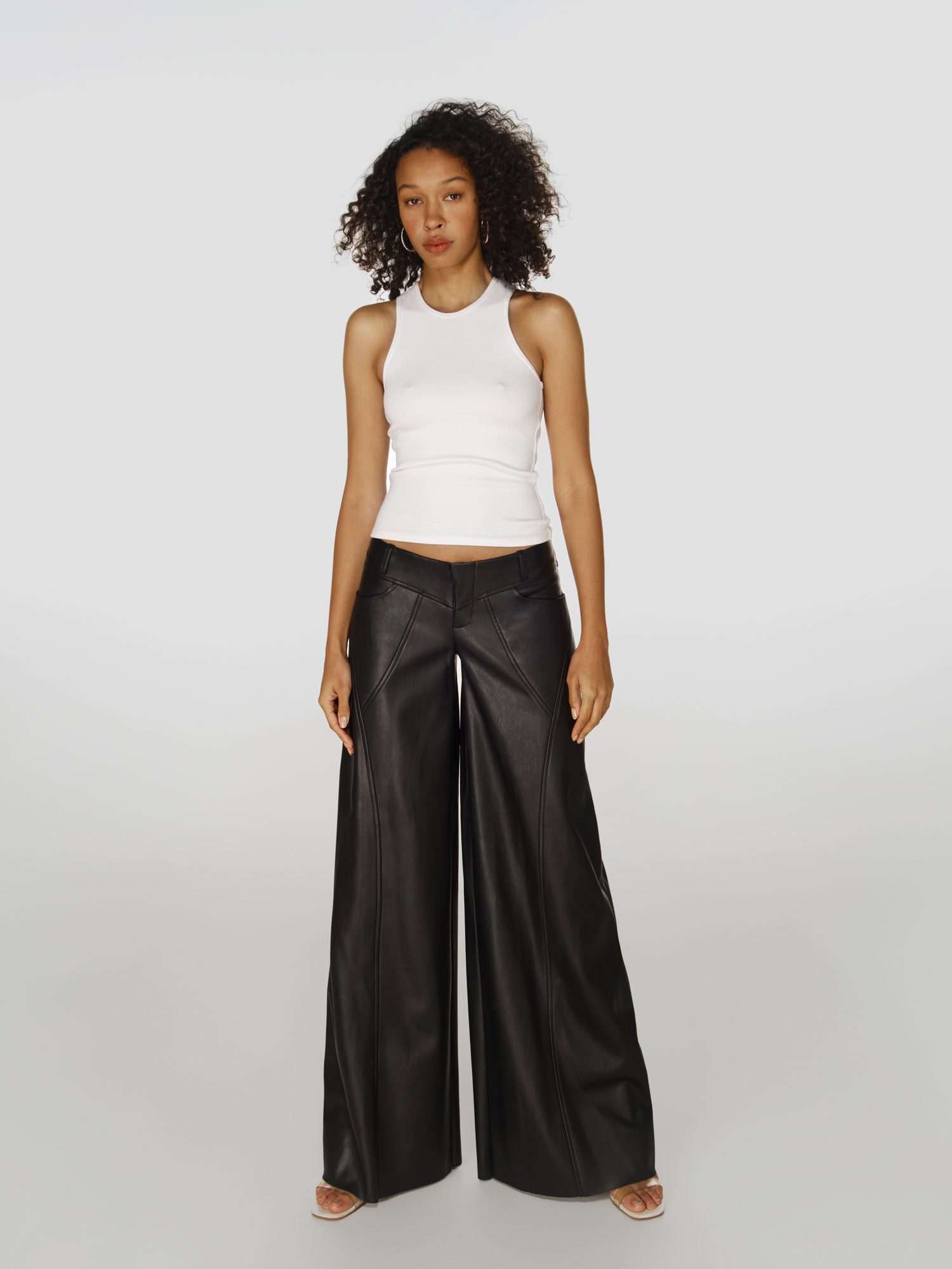 Full shot of a girl in a white viscose tank top and black vegan leather low rise wide leg pants