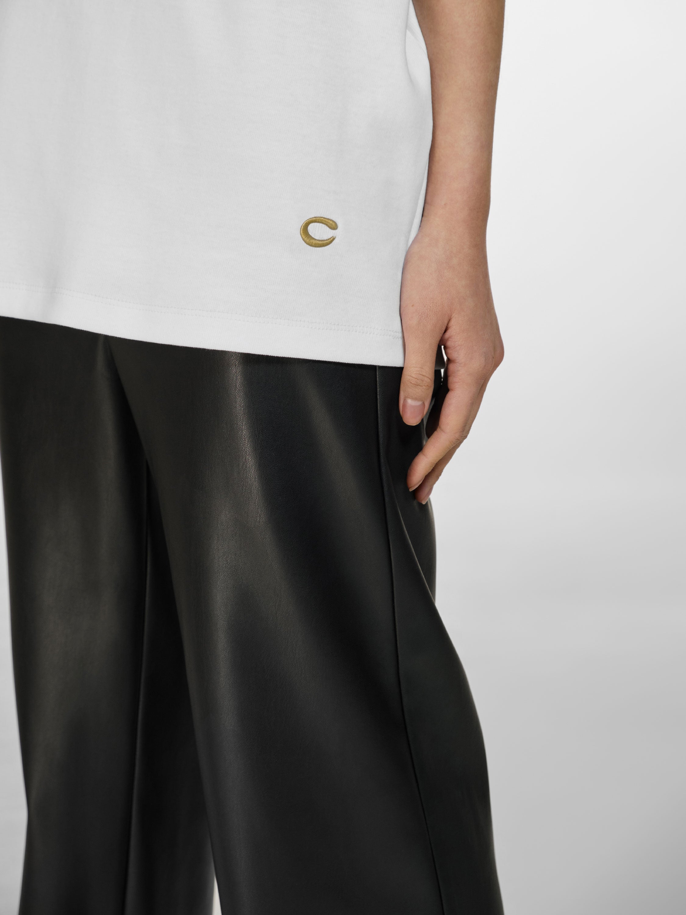 Medium closeup shot of a girl in a white cotton oversized t-shirt and black vegan leather straight leg pants