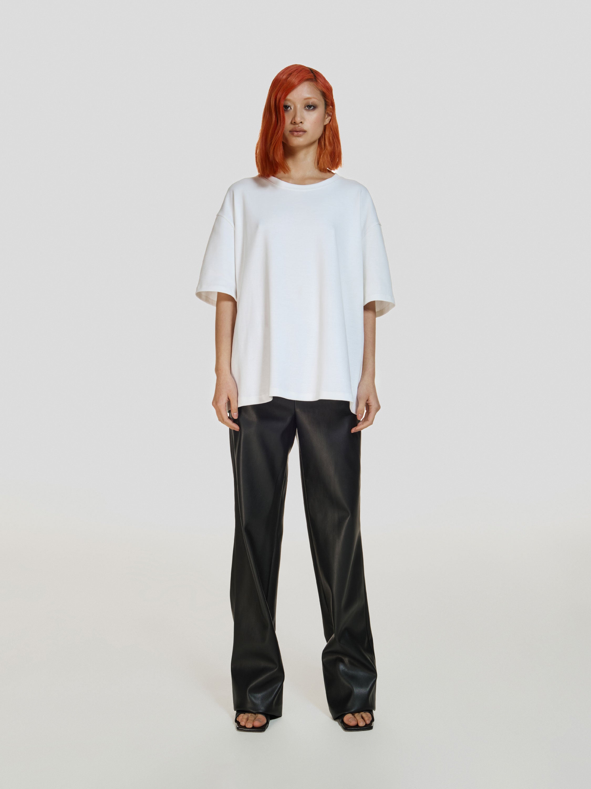 Full shot of a girl in a white cotton oversized t-shirt and black vegan leather straight leg pants