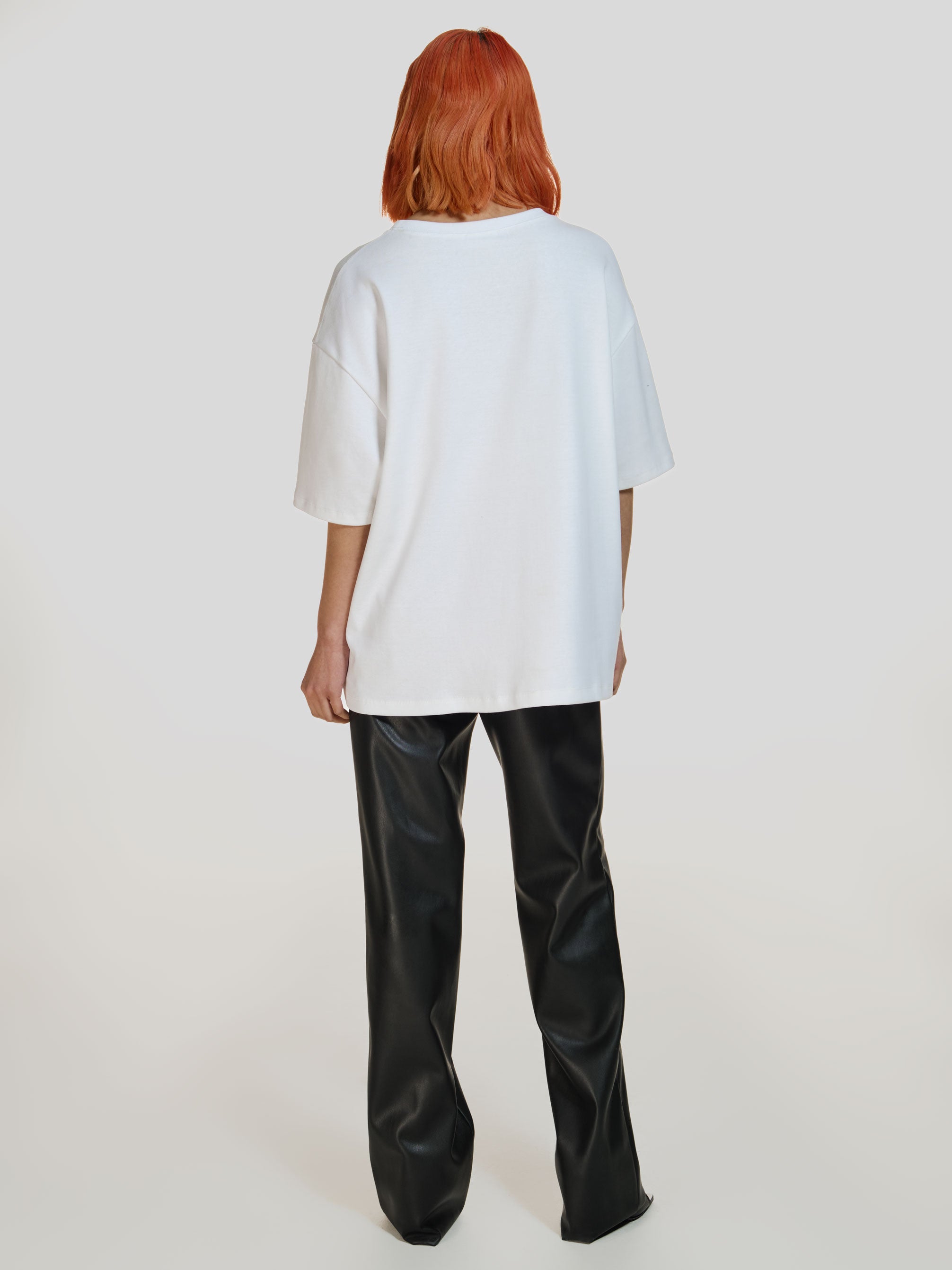 Full shot of a girl facing back in a white cotton oversized t-shirt and black vegan leather straight leg pants