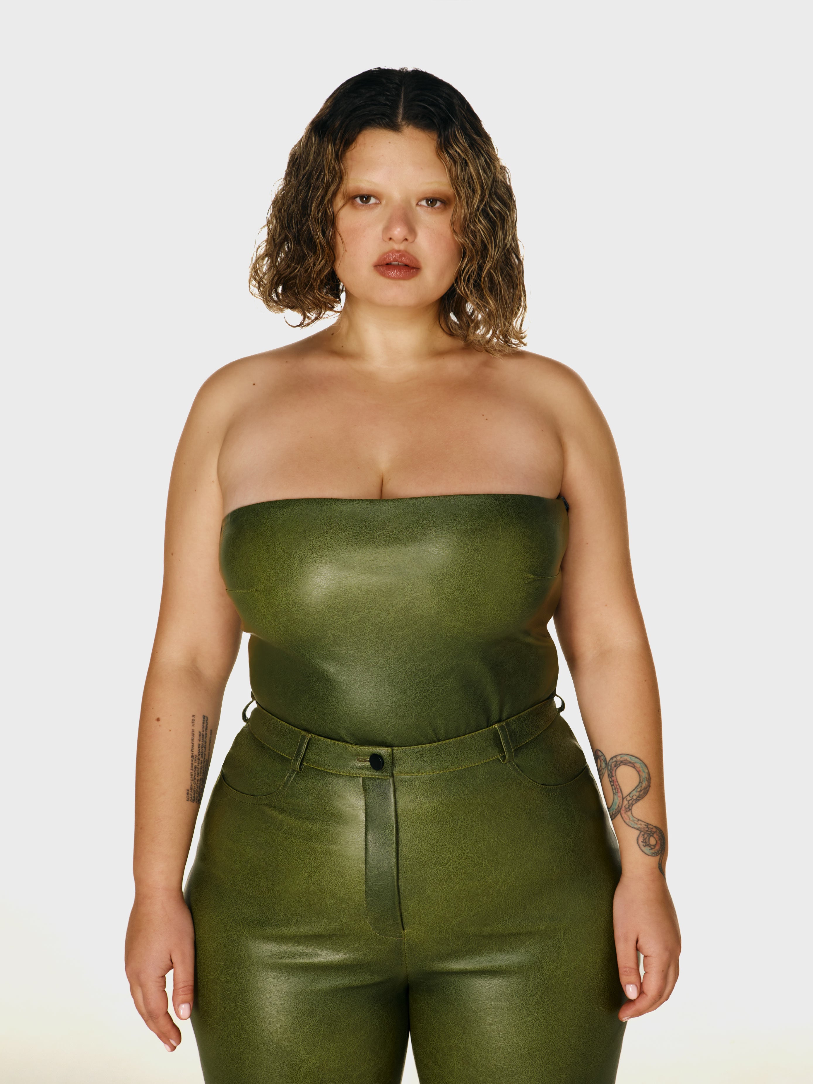 Cowboy shot of a girl in a green vegan leather tube top and green vegan leather high rise pants with straight leg
