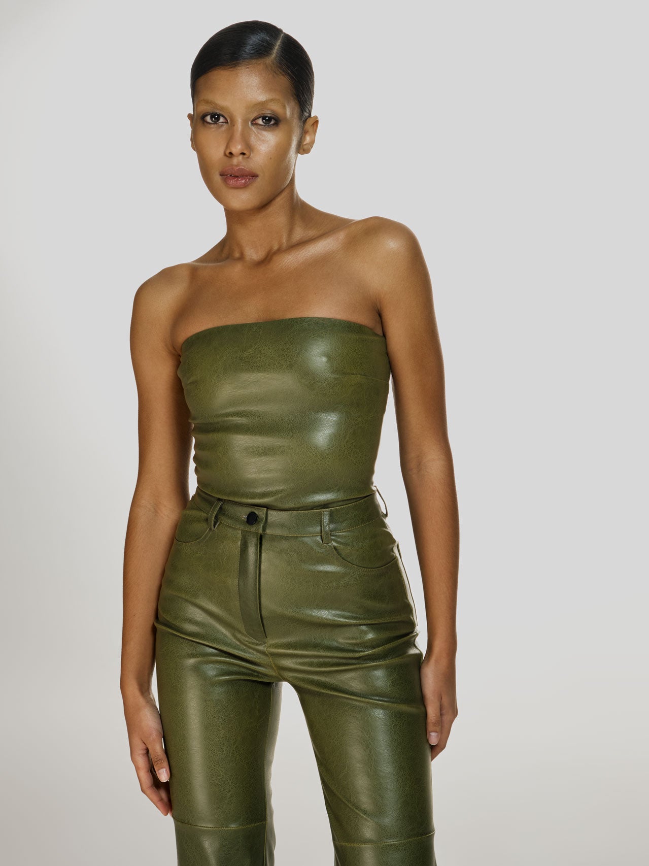 Cowboy shot of a girl in a green vegan leather tube top and green vegan leather pants with straight leg