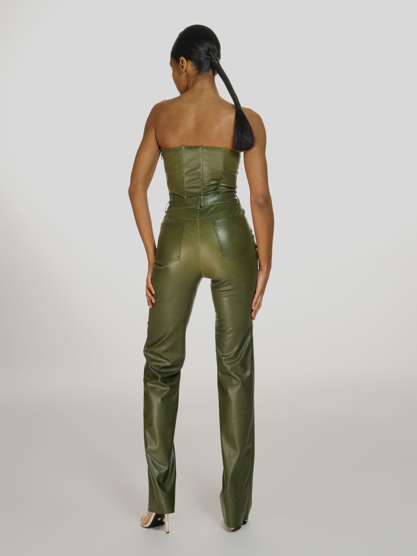 Full shot of a girl facing back in a green vegan leather tube top and green vegan leather high rise pants with straight leg