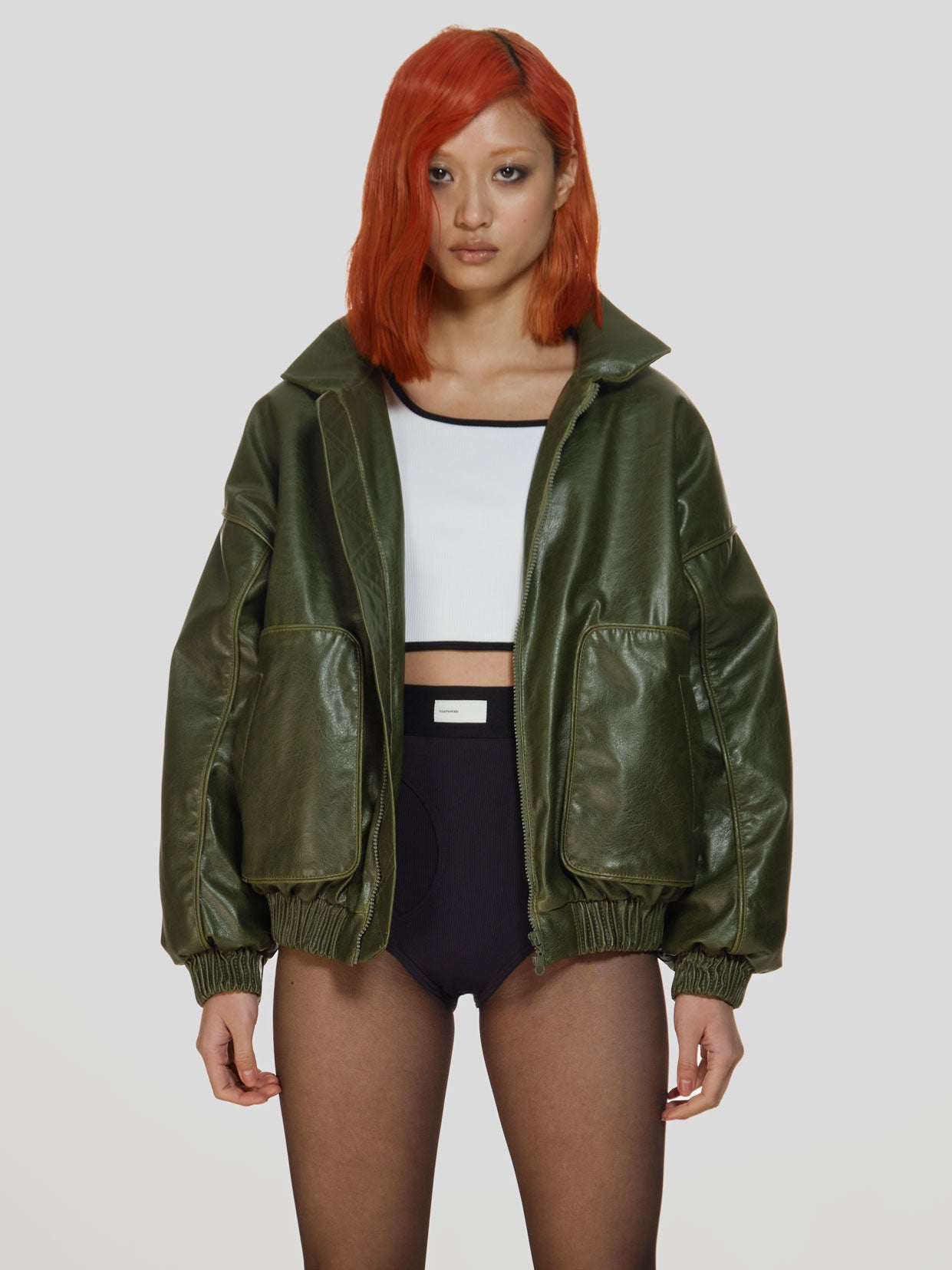 Cowboy shot of a girl in a green vegan leather oversized bomber, a white viscose crop top and black viscose high rise briefs