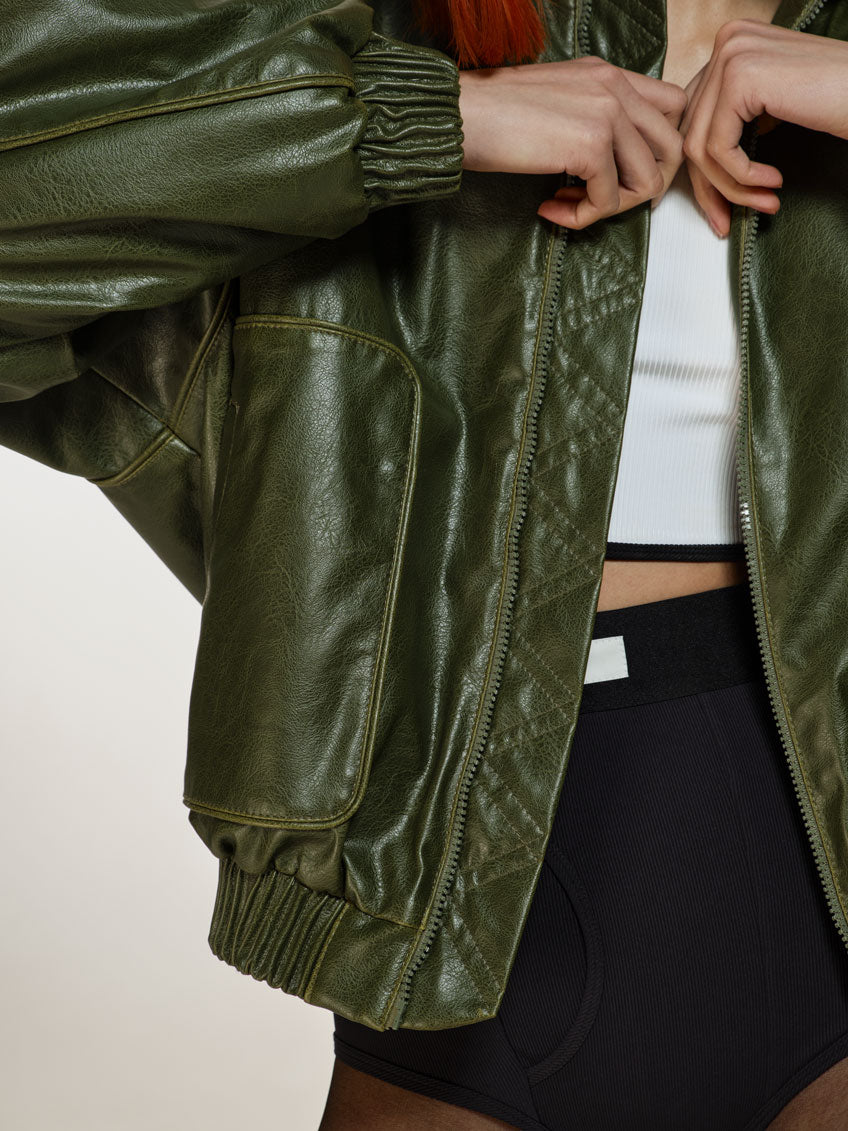 Closeup shot of a girl in a green vegan leather oversized bomber, a white viscose crop top and black viscose high rise briefs