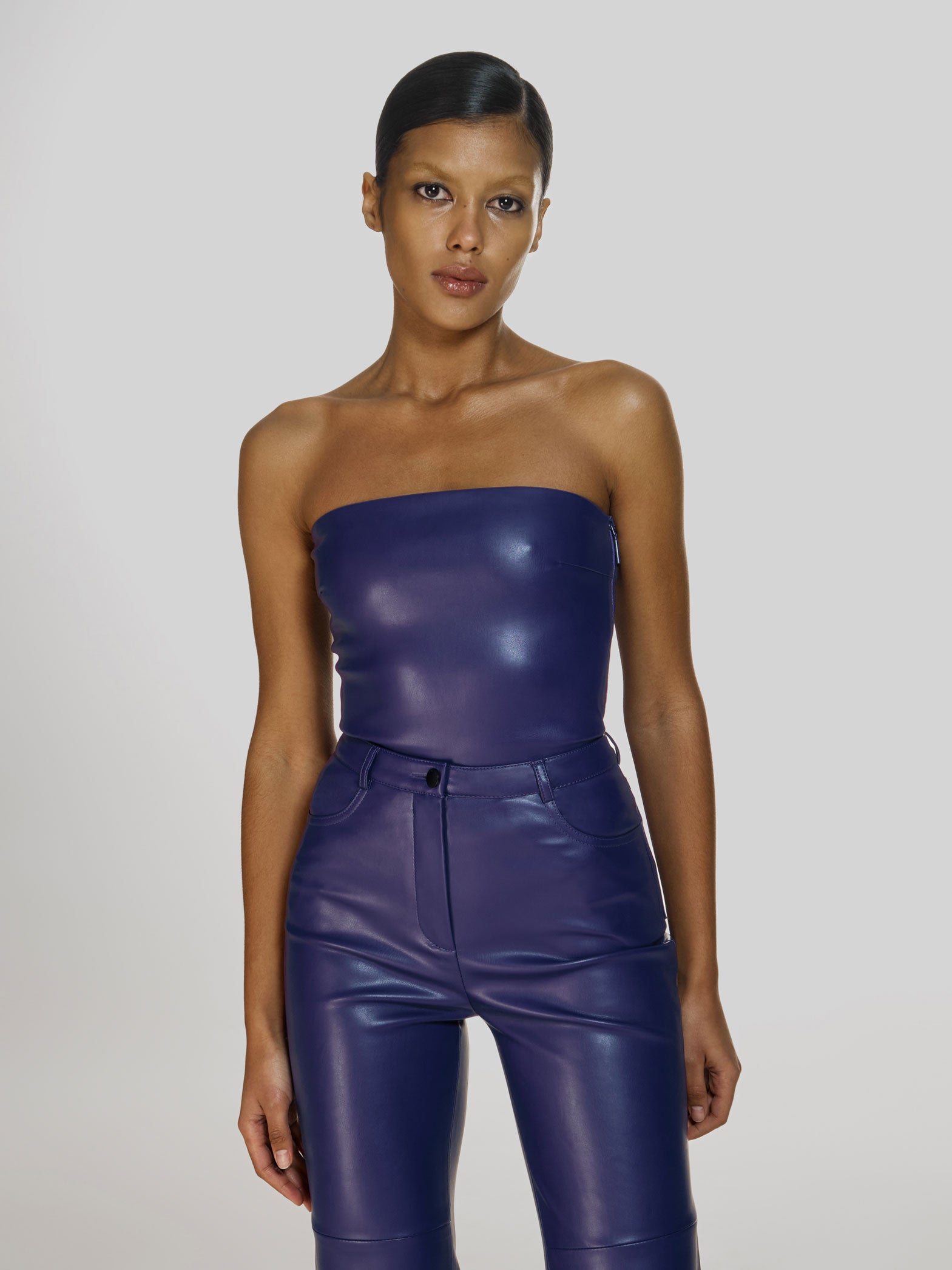 Cowboy shot of a girl in a purple vegan leather tube top and purple vegan leather high rise straight leg pants
