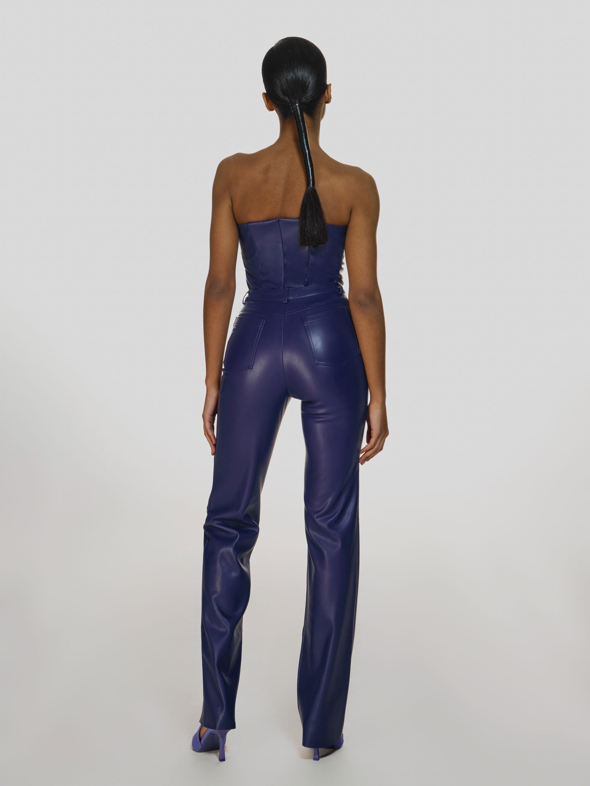 Full shot of a girl facing back in a purple vegan leather tube top and purple vegan leather high rise straight leg pants