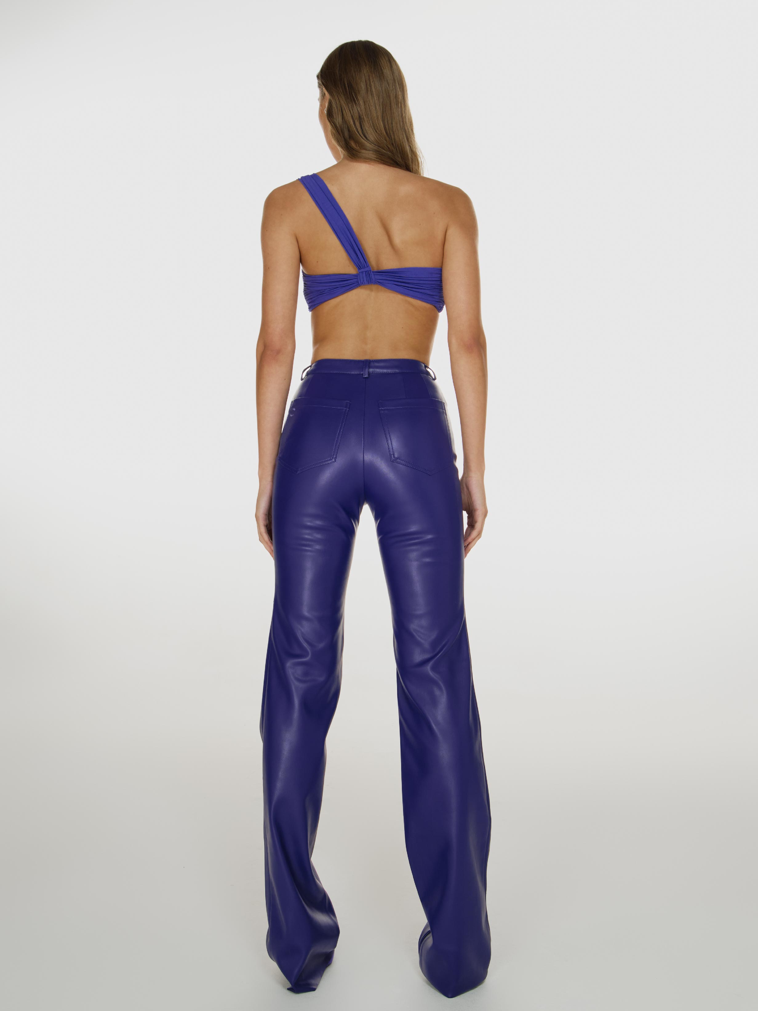Full shot of a girl facing back in a purple one shoulder crop top and purple vegan leather pants with straight leg